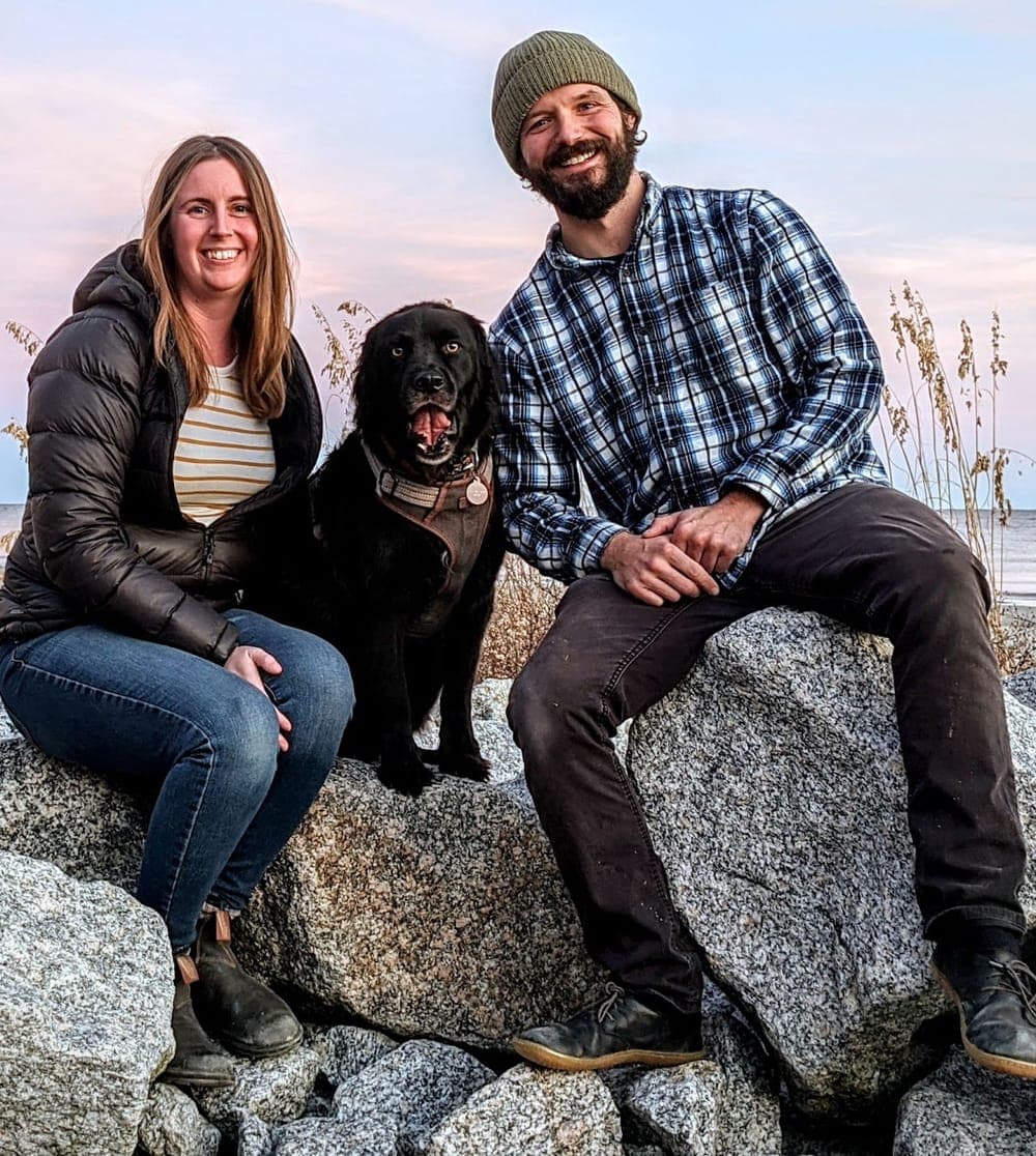 Spencer and Sara Clanin with their dog on the rocks by the coast